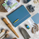 blue notebook and pencil with gardening tools and seeds arranged neatly
